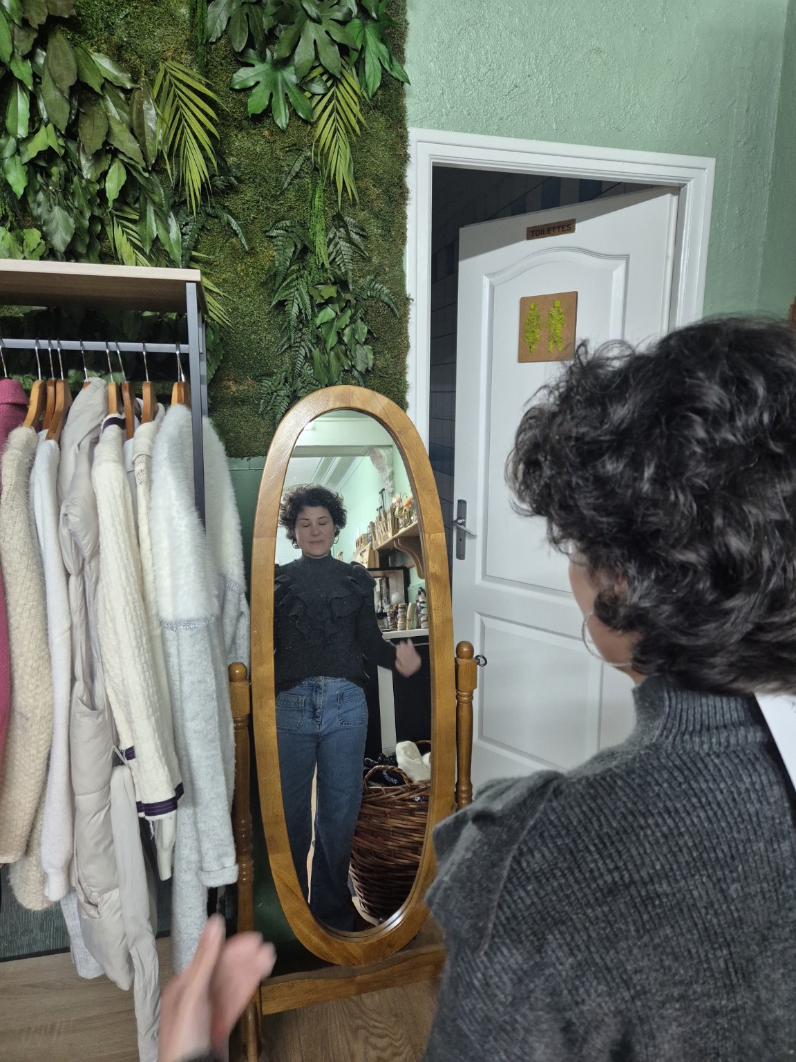 Cliente essayant une tenue devant un miroir, entourée de vêtements